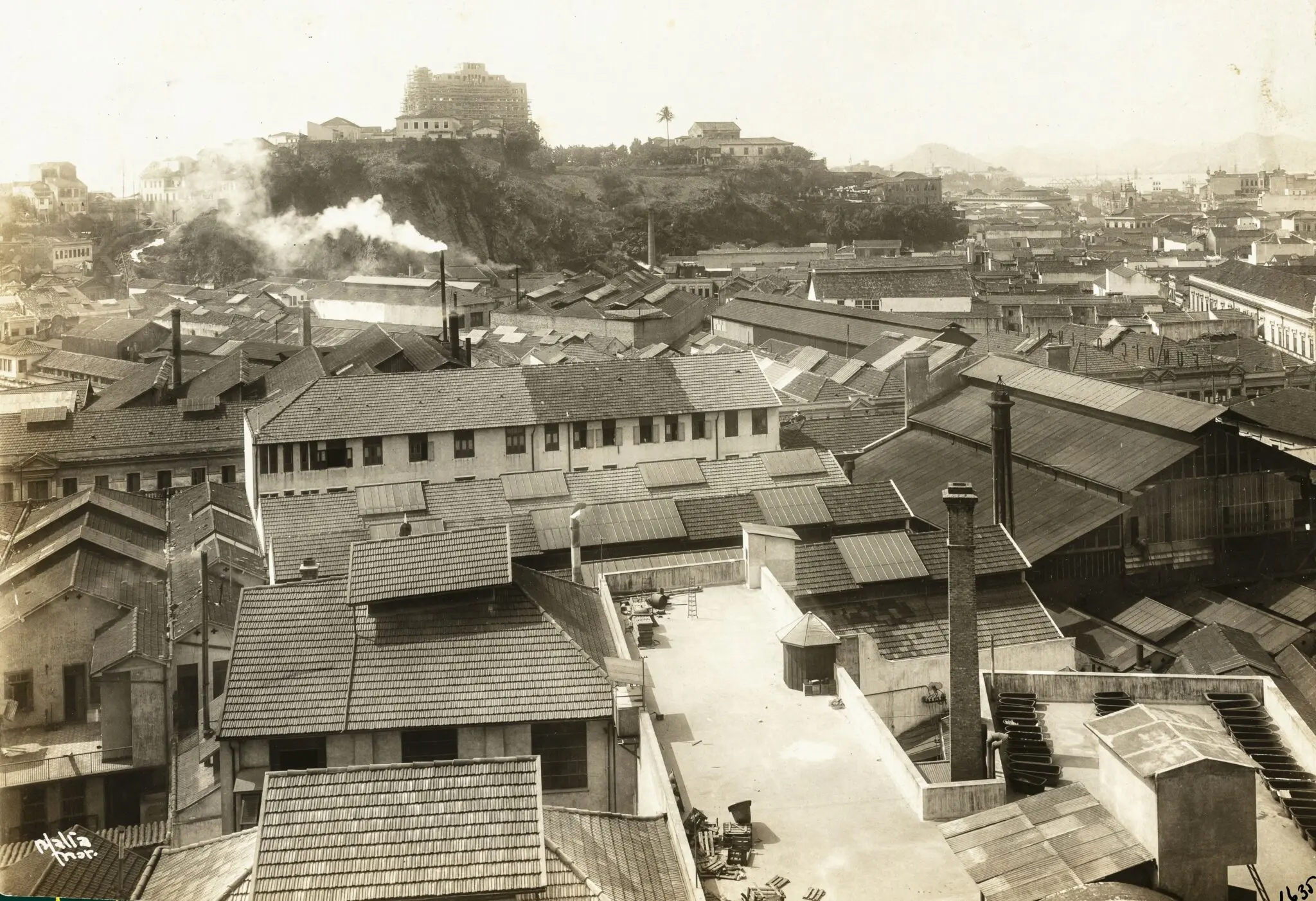Uma paisagem urbana densa em preto e branco, com casas, fábrica e colina.