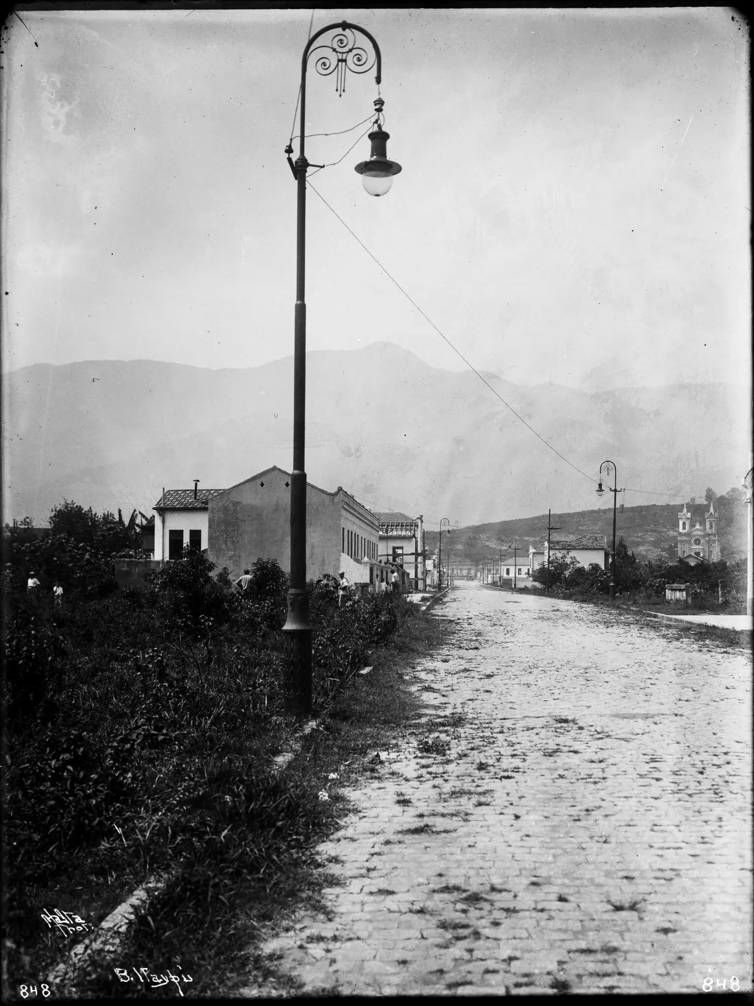 Rua histórica com iluminação pública e montanhas ao fundo.