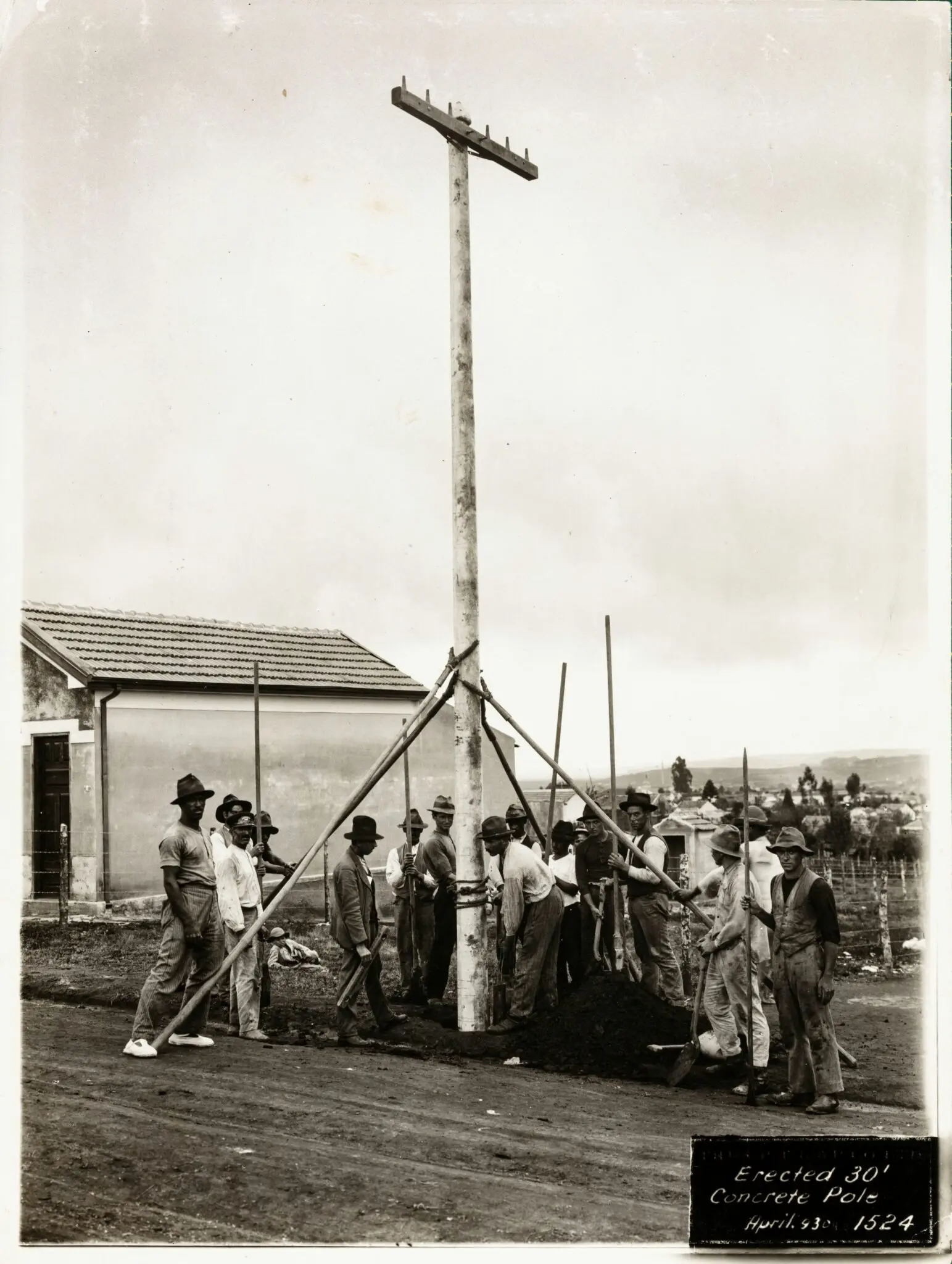 Trabalhadores erguendo poste de concreto em construção.