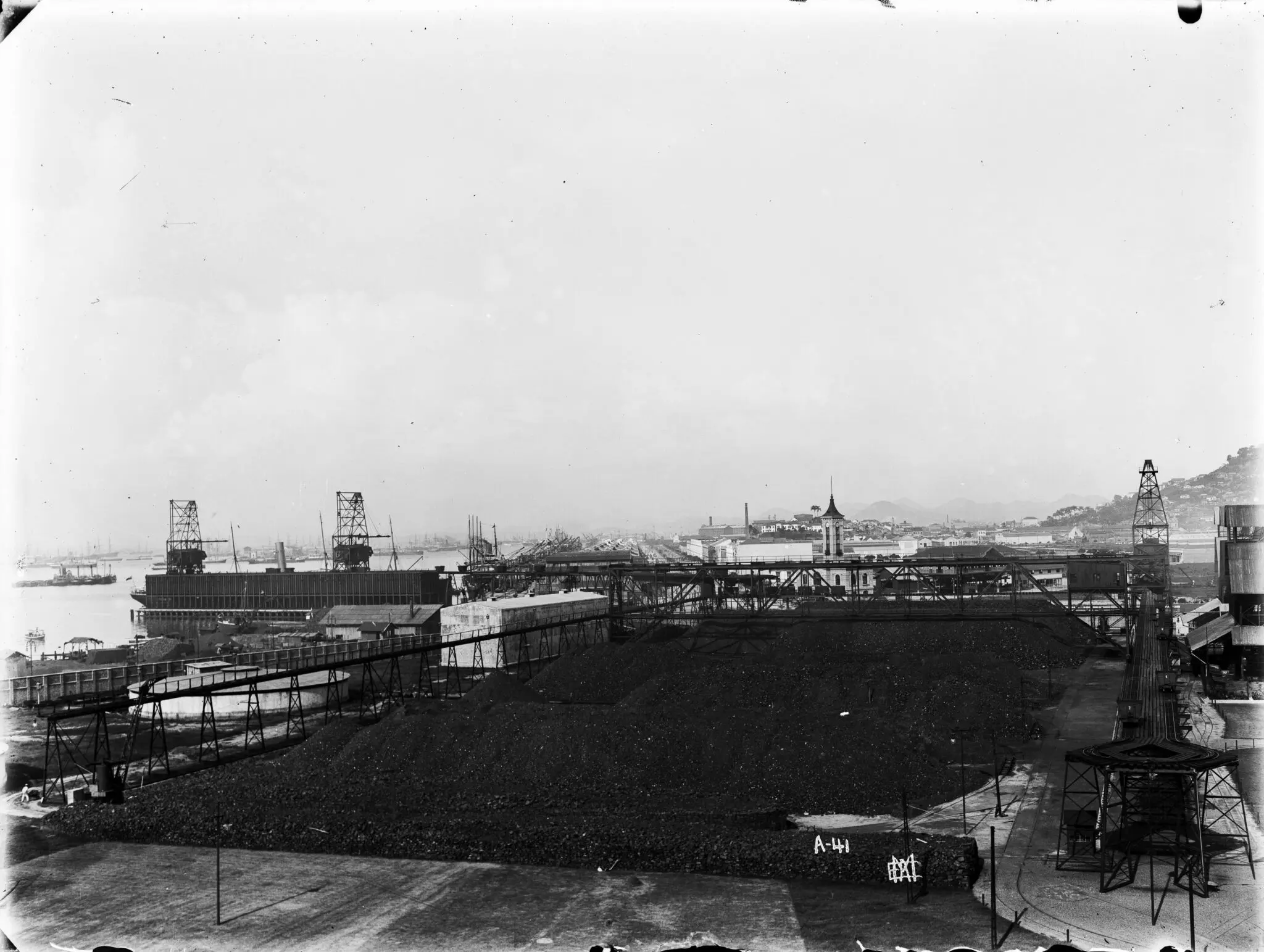 Área industrial com estruturas metálicas e pilha de material escuro.