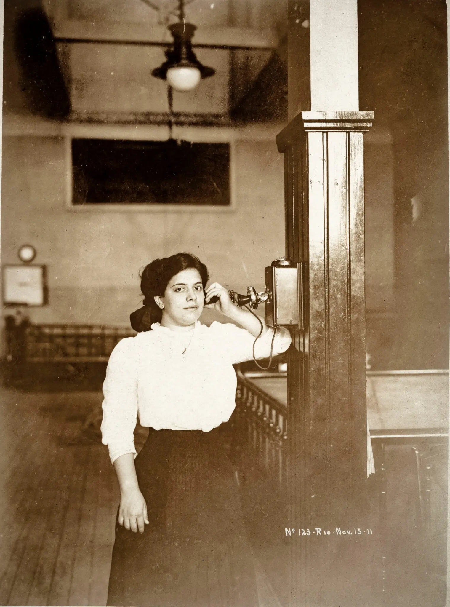 Mulher falando ao telefone em foto antiga em sepia.