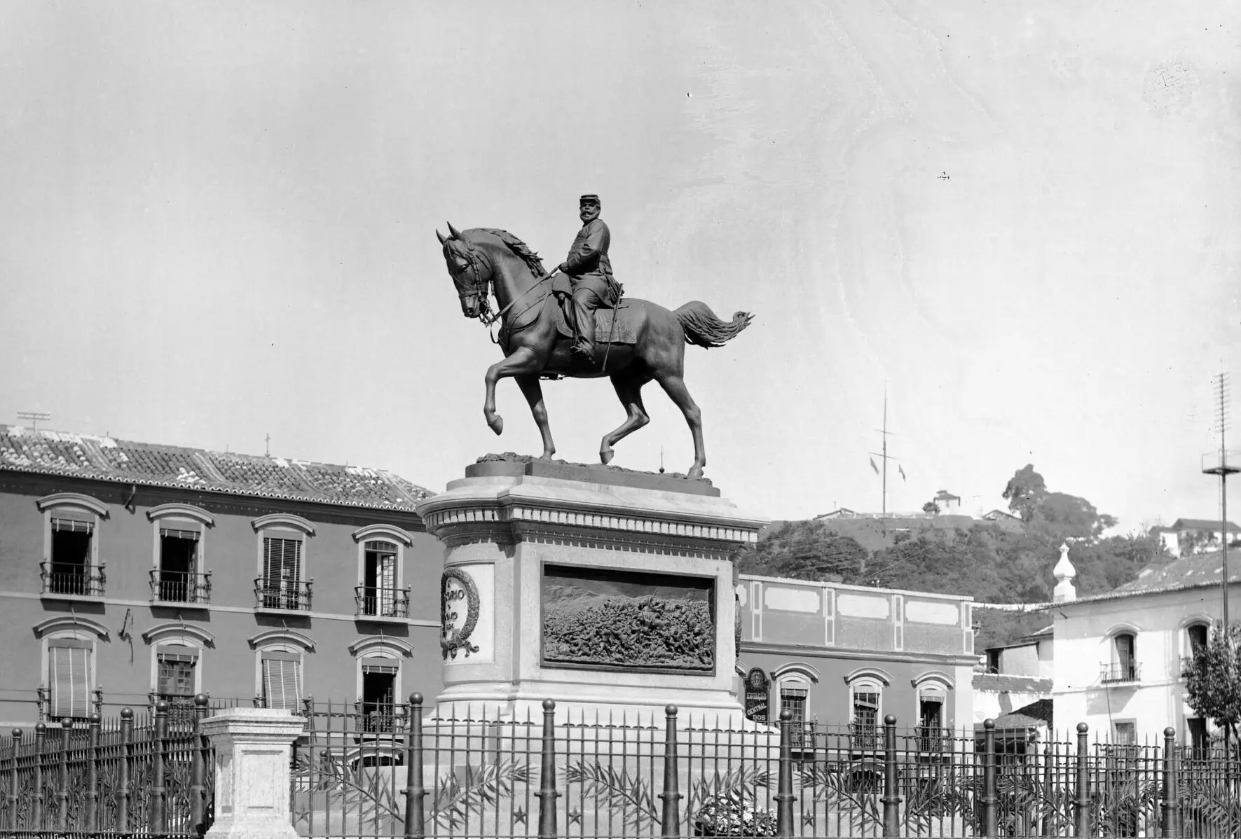 Estátua equestre em preto e branco, soldado e cavalo, edifícios históricos ao fundo, Morro do Castelo à direita.