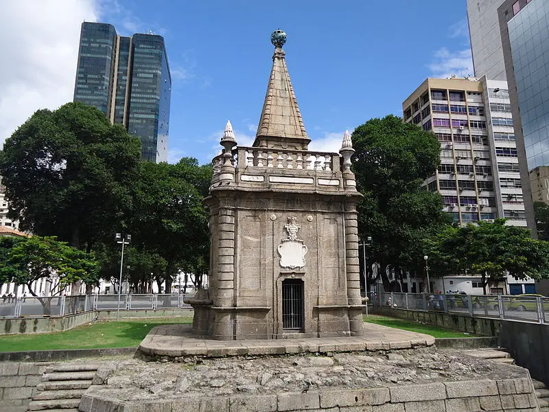 Chafariz histórico em espaço público com telhado piramidal.