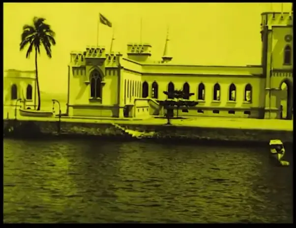 Palácio antigo ao lado do mar com palmeira e torres pontiagudas.
