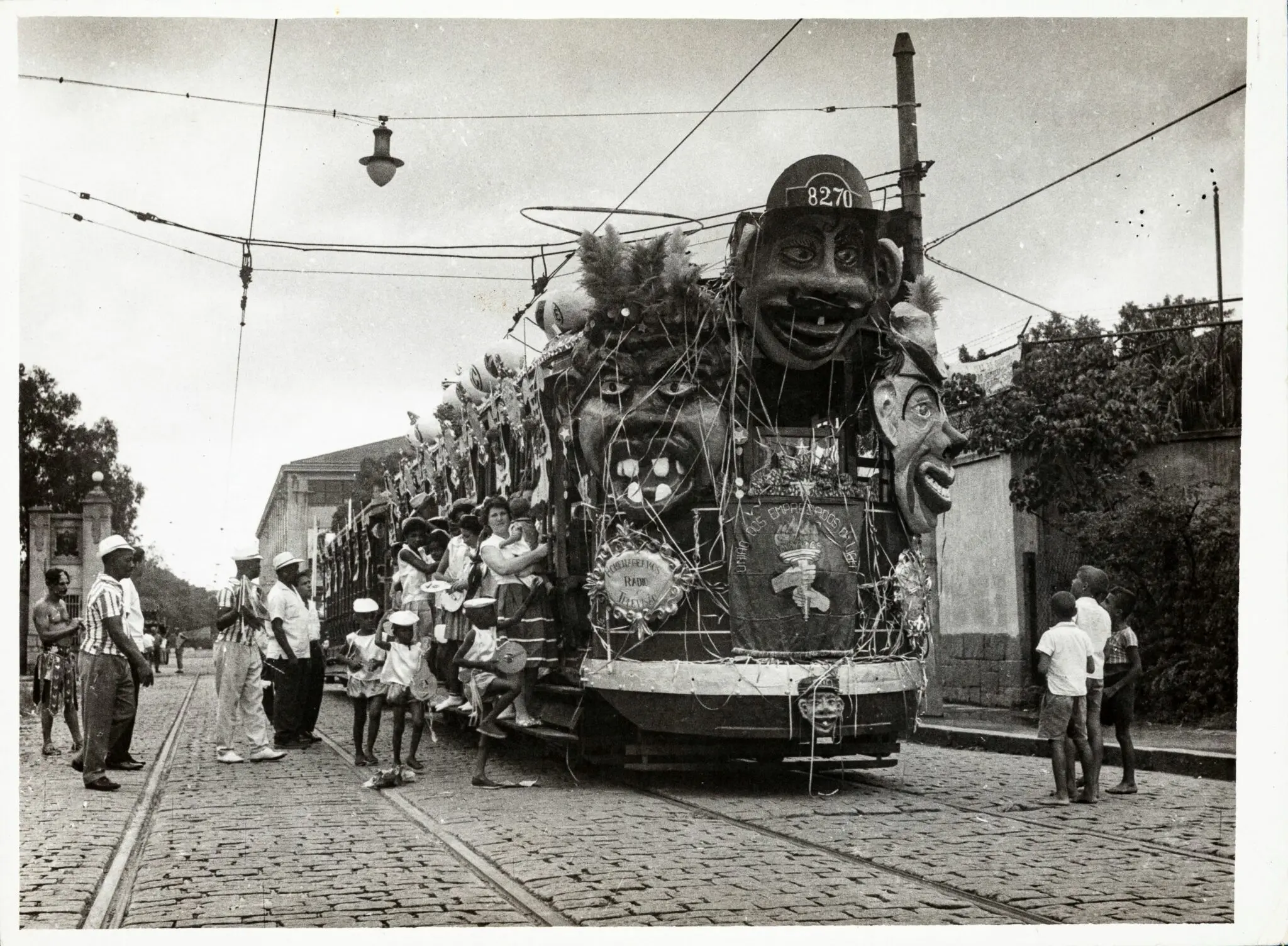 Trem festivo em desfile de Carnaval, com espectadores observando.