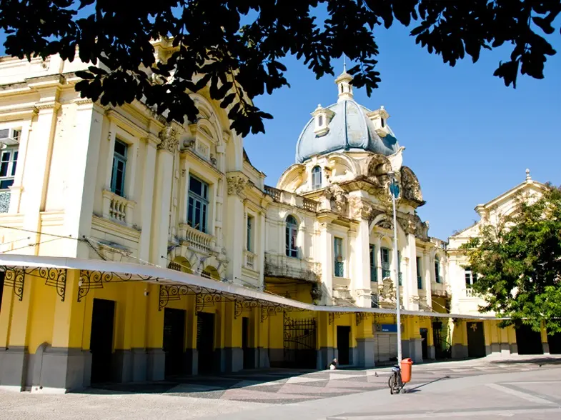 Estação ferroviária histórica com edifício amarelo e detalhes ornamentais azuis e brancos.