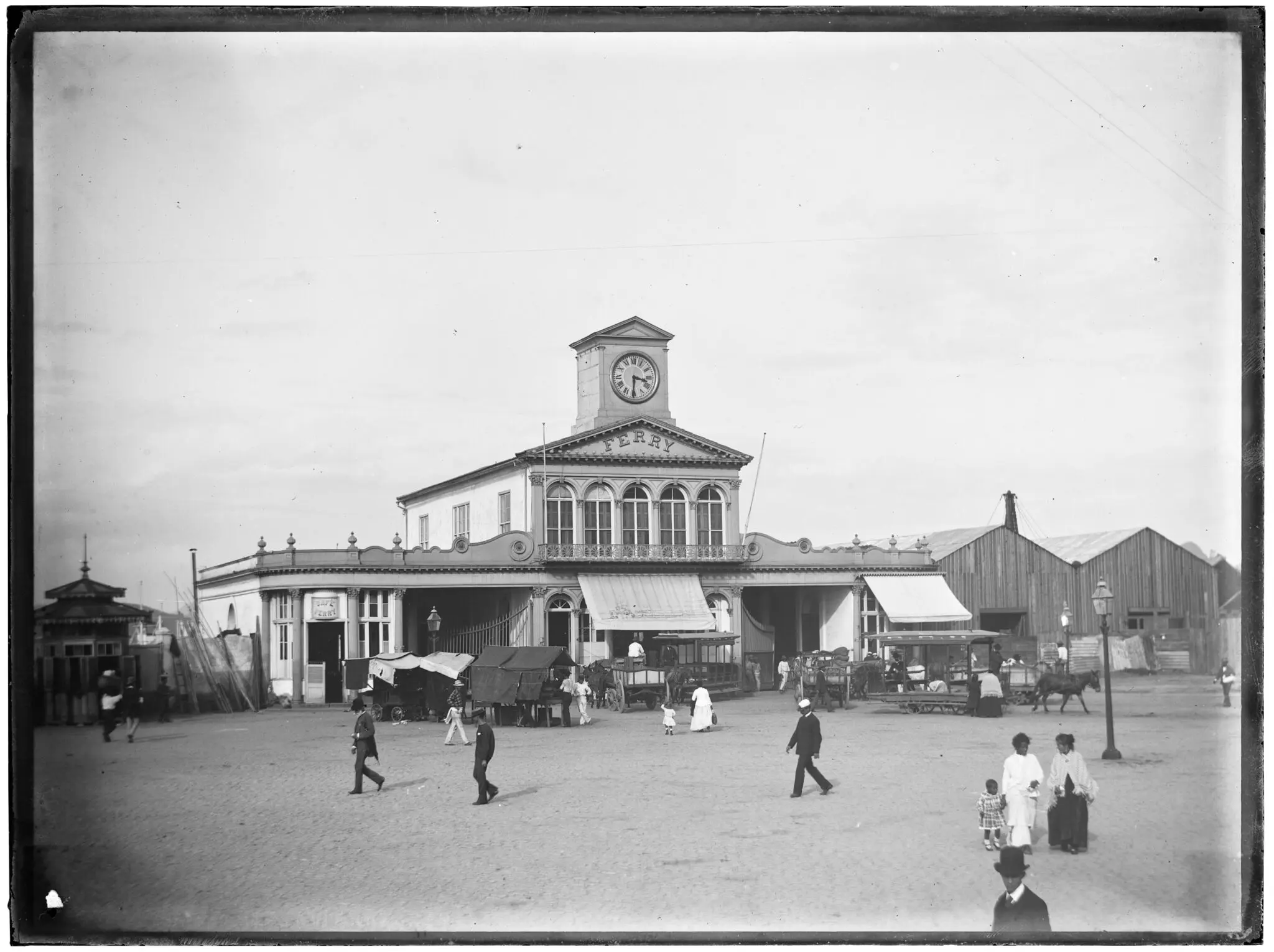 Estação de ferry antiga com edifício central e torre, arco à esquerda e construção de madeira à direita.