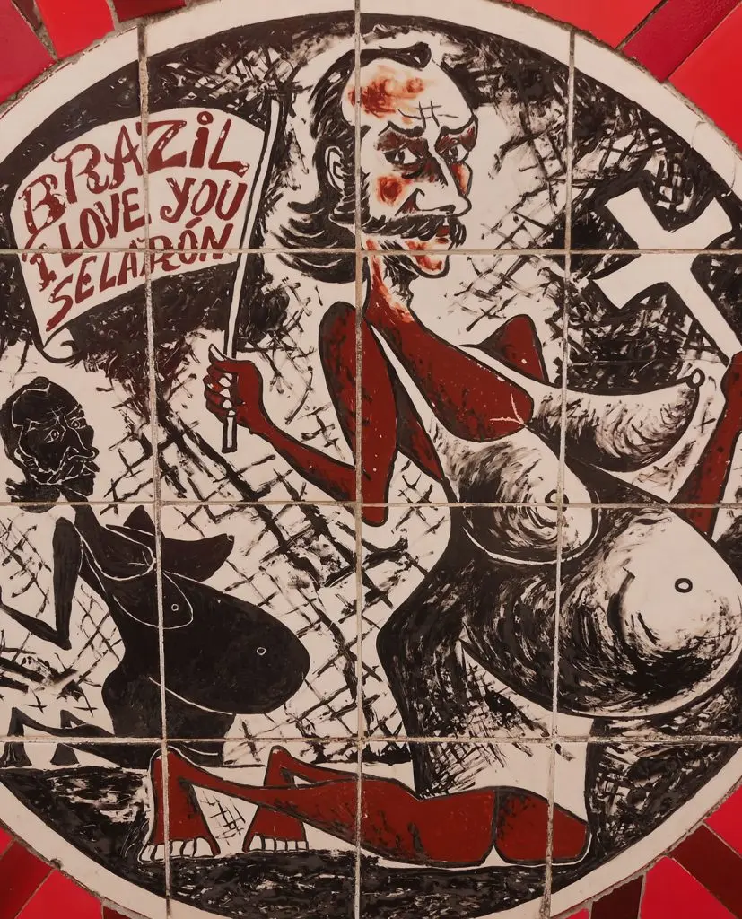 Pintura circular em preto, branco e vermelho, retratando rosto humano segurando cartaz.