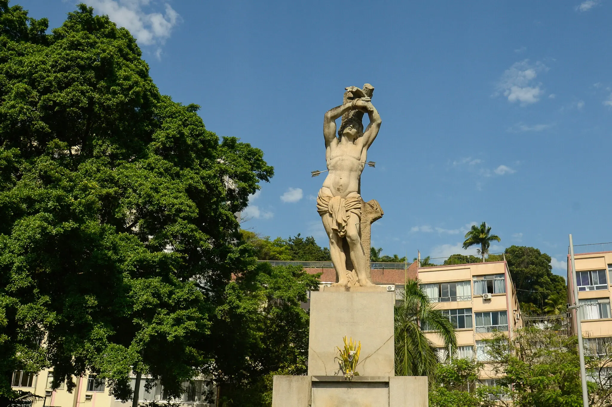 Monumento em praça com estátua de homem segurando animal morto.