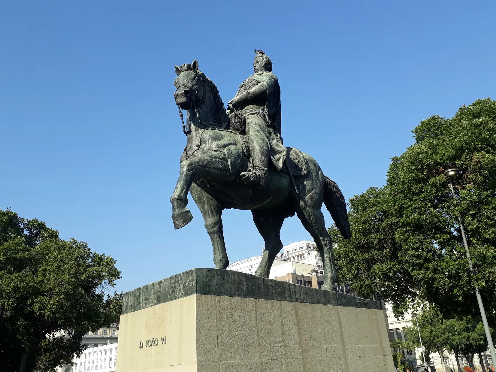 Estátua equestre em movimento, centro urbano, céu azul claro.