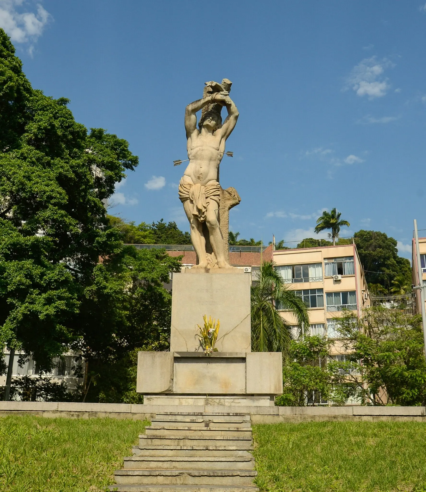 Monumento em praça com estátua de homem nu segurando figura menor.