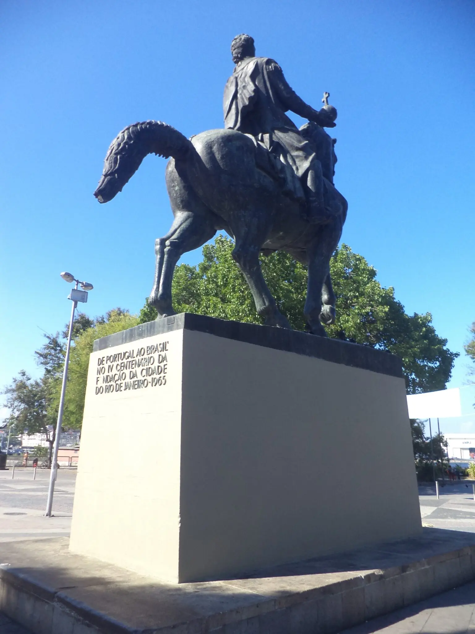 Estátua equestre em movimento, céu azul e árvores verdes ao fundo.