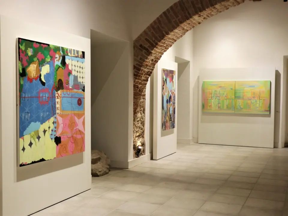 Três quadros coloridos em uma galeria de arte dentro de um convento.