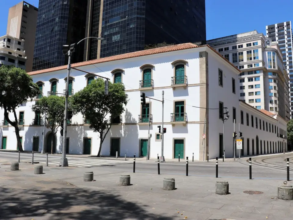 Edifício histórico em cidade moderna, árvore verde, prédios brancos e de vidro.