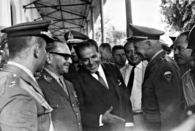 Reunião social ou oficial em local coberto, com militares e ternos.