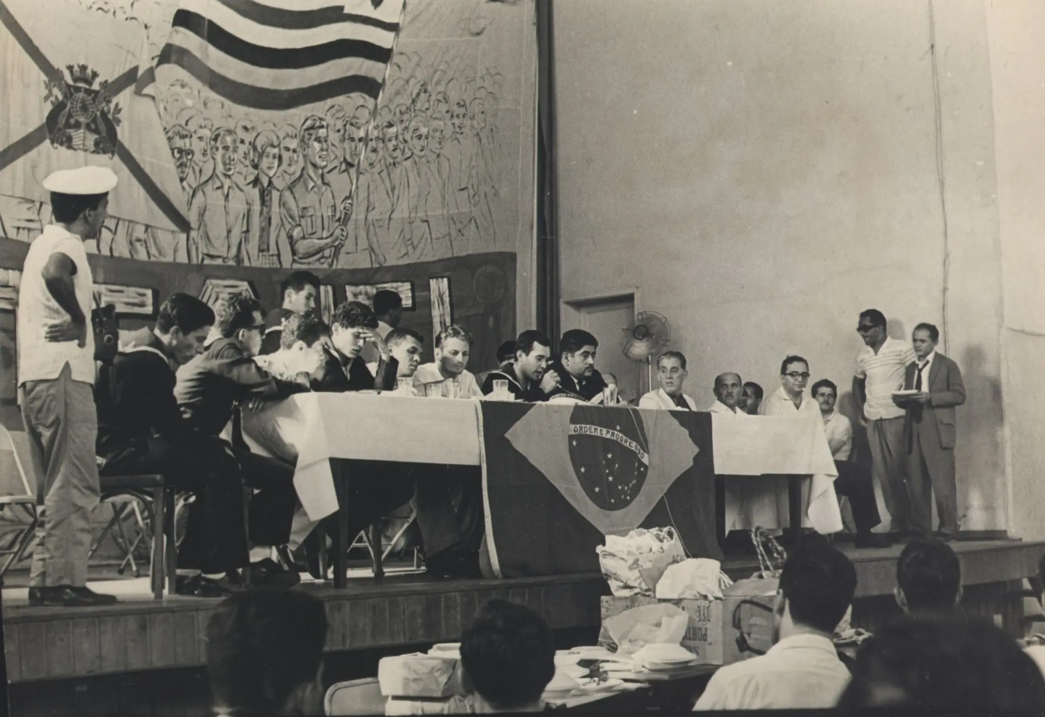 Evento público com bandeira e pessoas em palco.