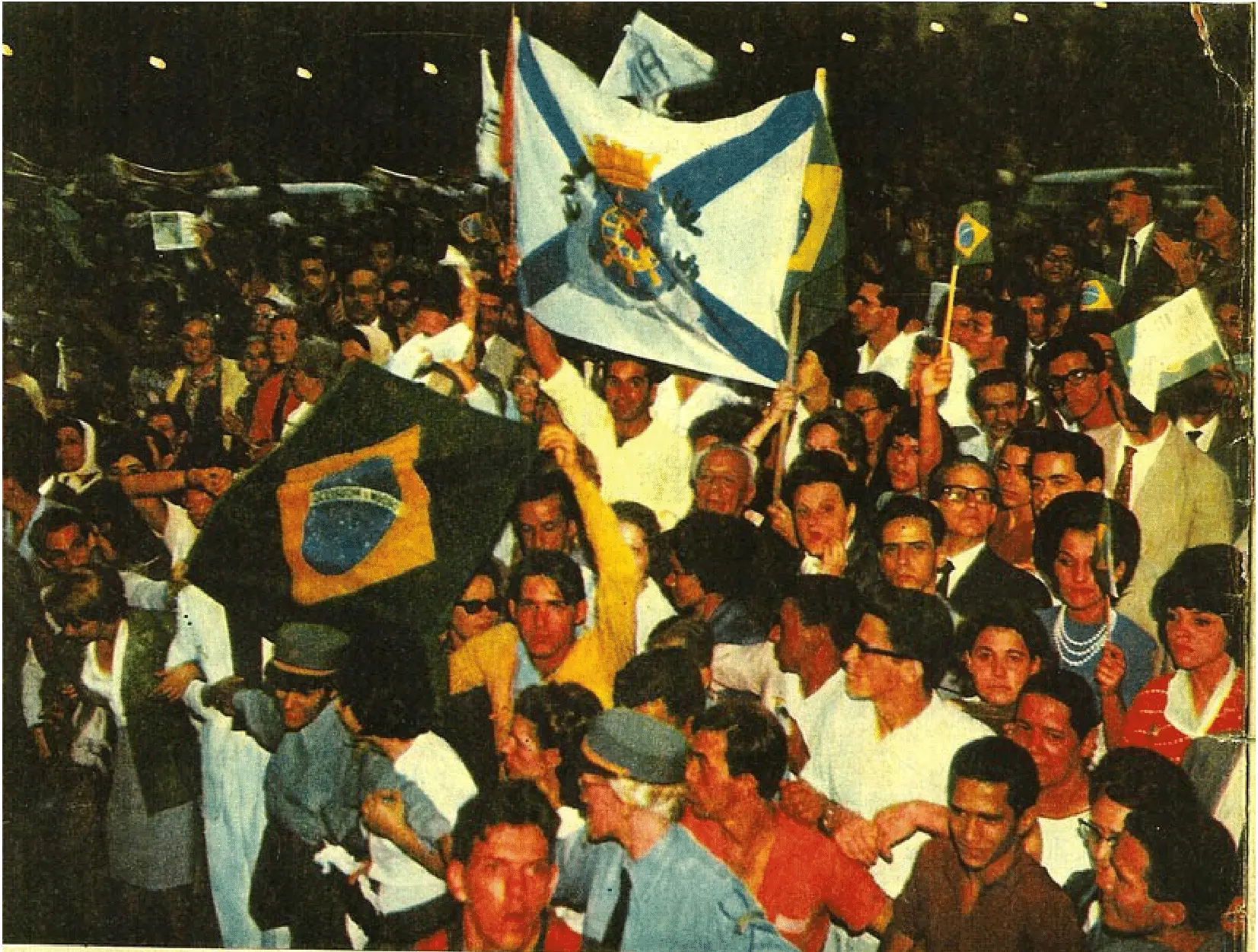Multidão animada com bandeiras em evento noturno.