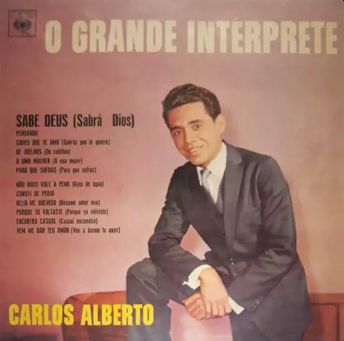 Capa de álbum musical com teto marrom, título "O GRANDE INTERPRETE", músicas em português e espanhol, pessoa em terno azul escuro sentada em cadeira vermelha.