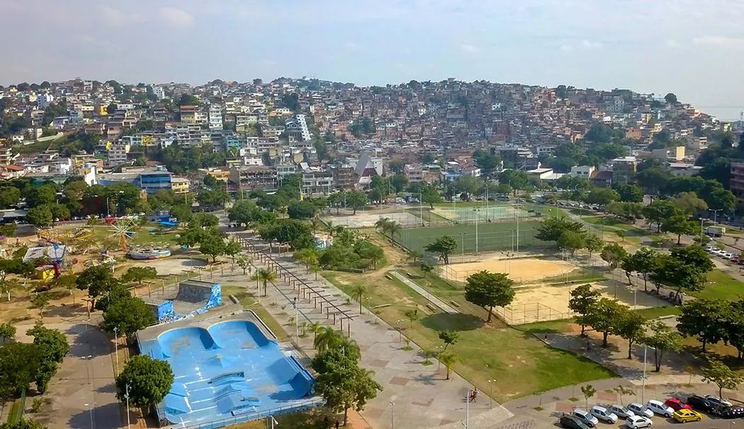 Favela em colina íngreme, parque e skatepark abaixo, futebol e carrossel à volta.