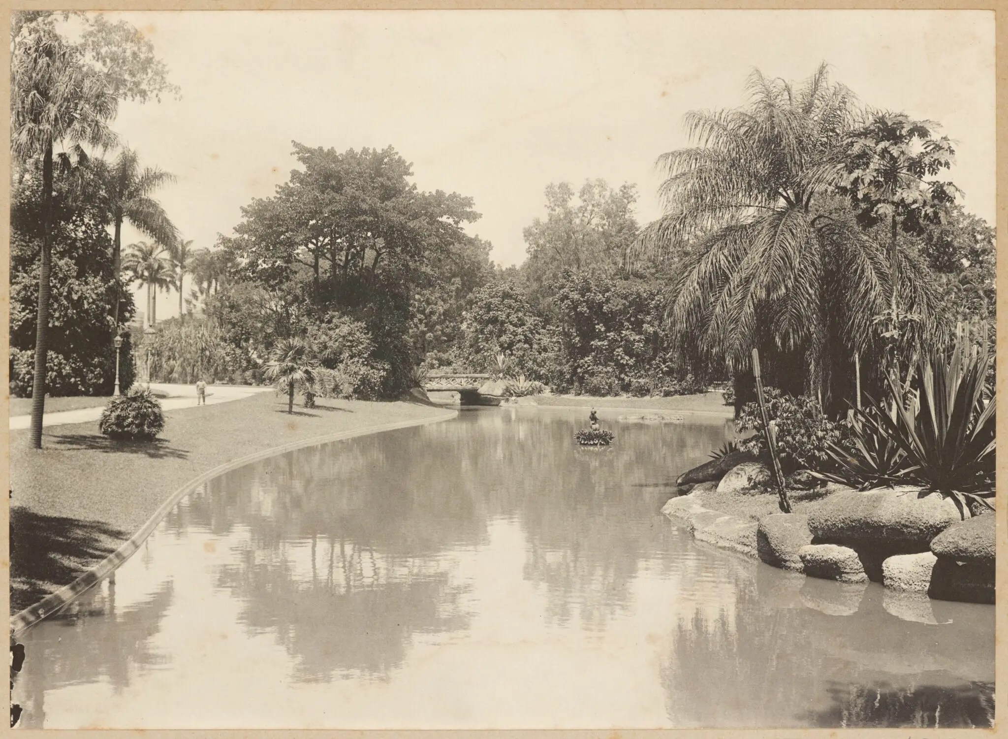 Parque antigo com lago, árvores e ponte.