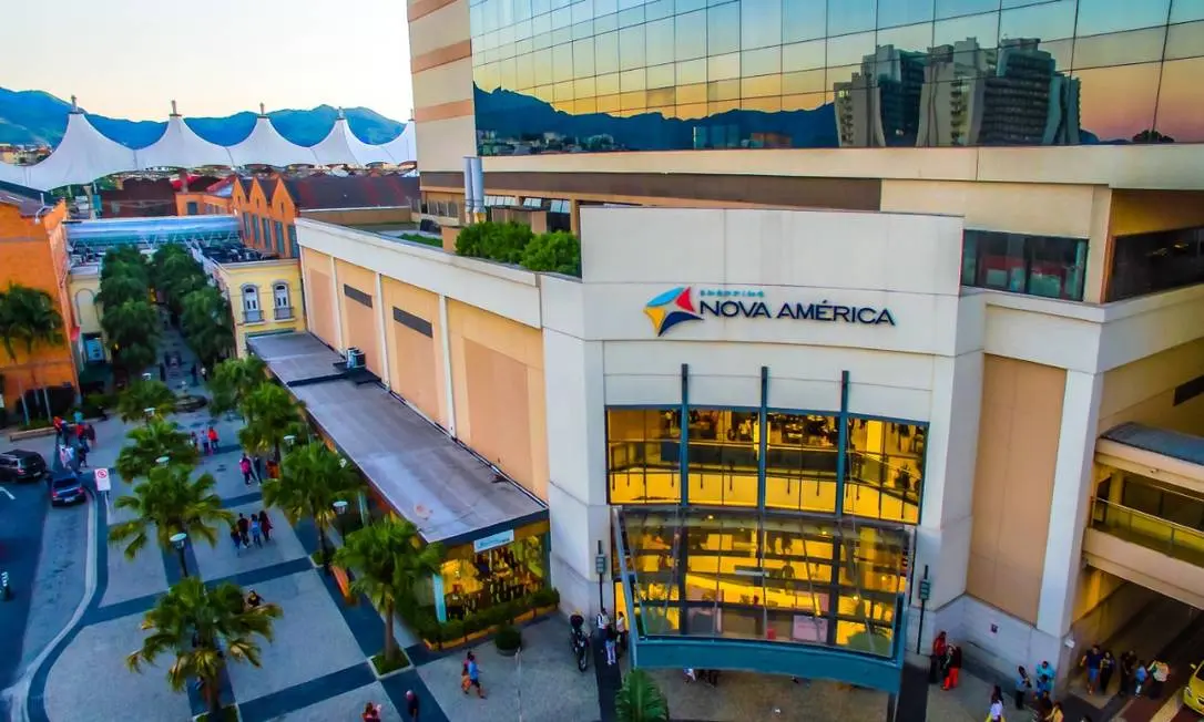 Shopping Nova América visto aéreo com palmeiras e edifício de vidro e alvenaria.
