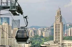 Teleférico em cidade com edifícios modernos e montanhas verdes ao fundo.