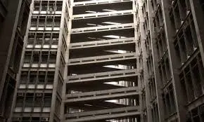 Edifício moderno com estacionamento, estrutura metálica complexa, preto e branco.