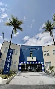Prédio moderno com fachada azul e branco, palmeiras e clínica da família do Caju.