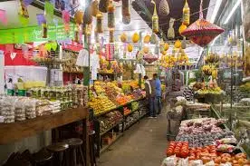 Mercado local com barracas de frutas e verduras, variedade de alimentos em caixas e prateleiras.