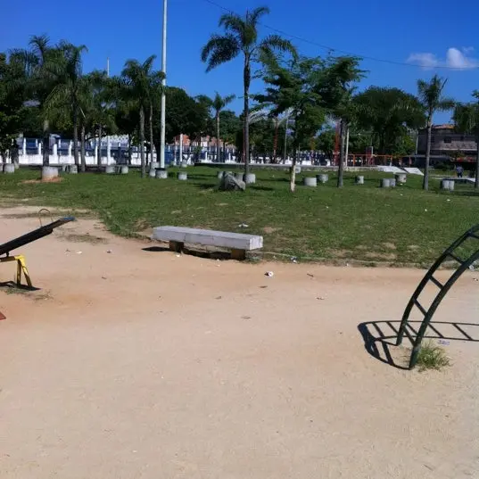 Praça com árvores de palmeira, bancos e estruturas metálicas.