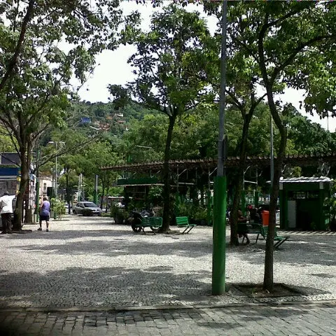 Praça Barão de Drumond com árvores, pavilhão verde e pessoas caminhando.