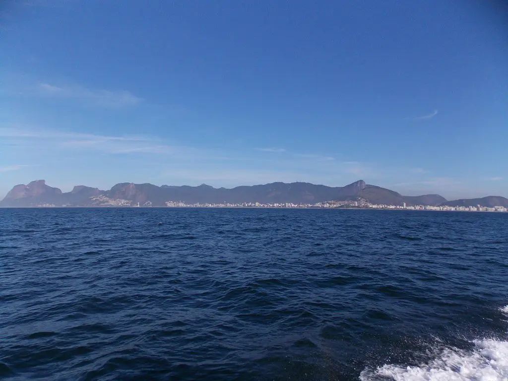 Cenário marinho com montanhas e cidade ao fundo.