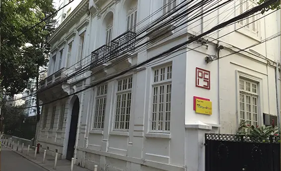 Prédio antigo com fachada branca e árvore verde à esquerda.