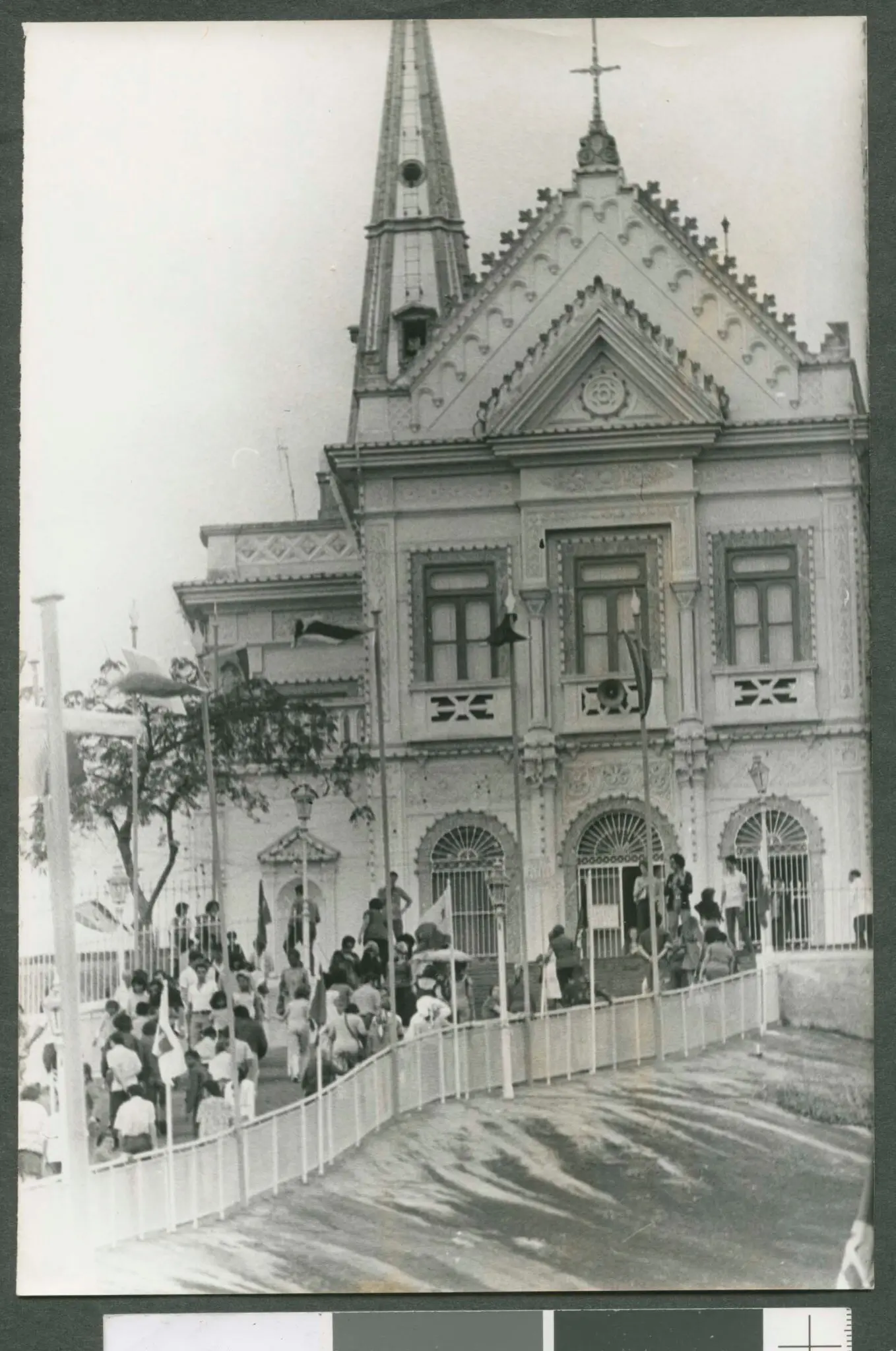 Basílica gótica com árvores e pessoas reunidas.