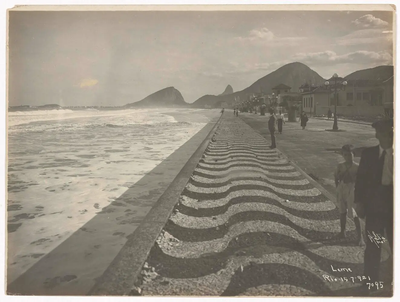 Calçadão costeiro com mar e pessoas caminhando.