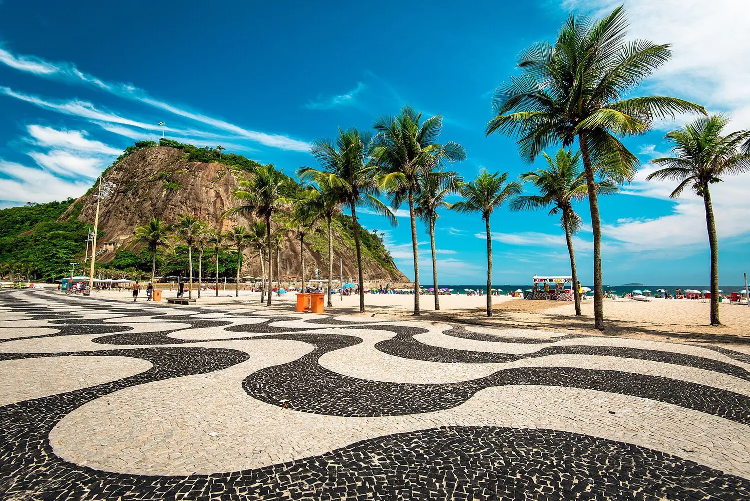 Calçadão de Copacabana com praia, palmeiras, padrão geométrico e colina verde.