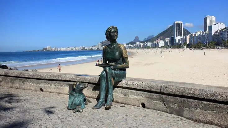 Estátua feminina com cachorro em praia costeira.