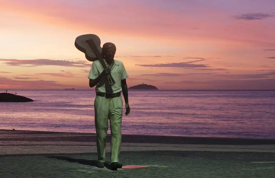 Estátua de Tom Jobim em praia durante pôr-do-sol.