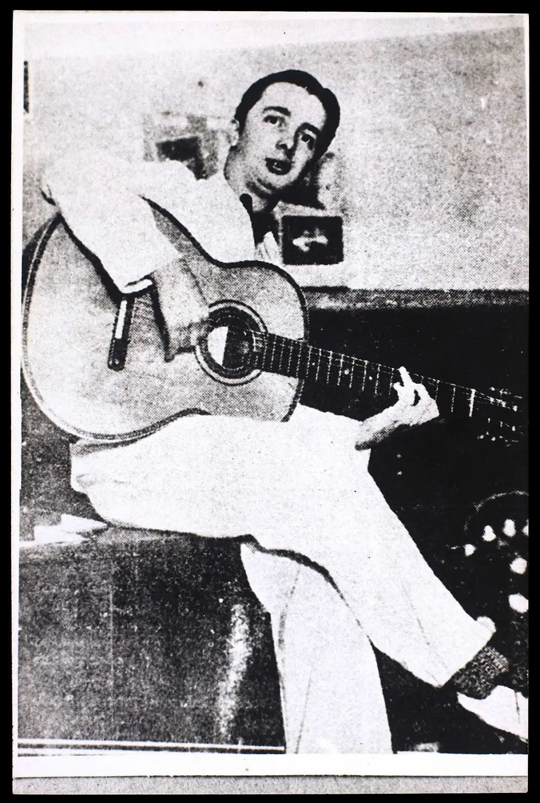Homem toca guitarra acústica em preto e branco.