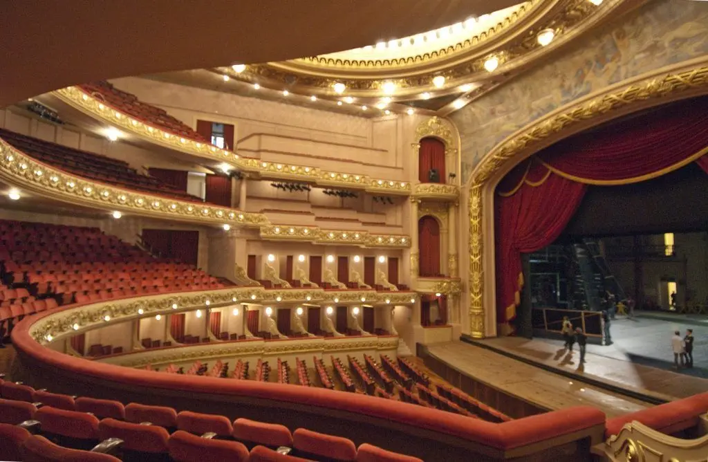 Teatro com cadeiras vermelhas e palco adornado.