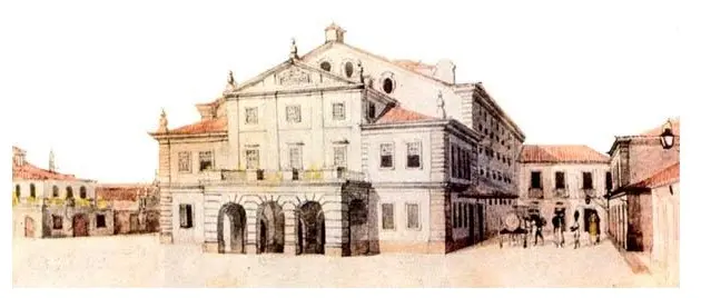 Teatro antigo em praça com mercado e igreja ao fundo.