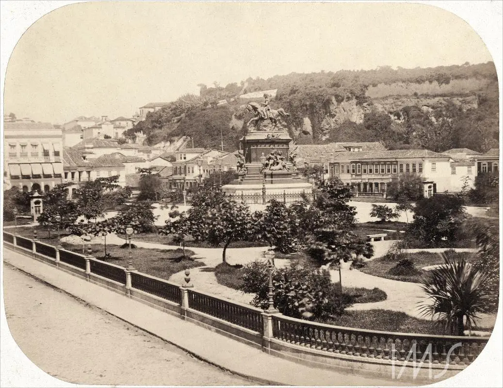 Parque histórico com estátua central e edifícios históricos ao fundo.
