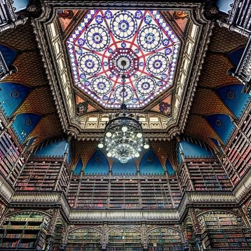 Interior de biblioteca histórica com teto octogonal e vitrais coloridos.