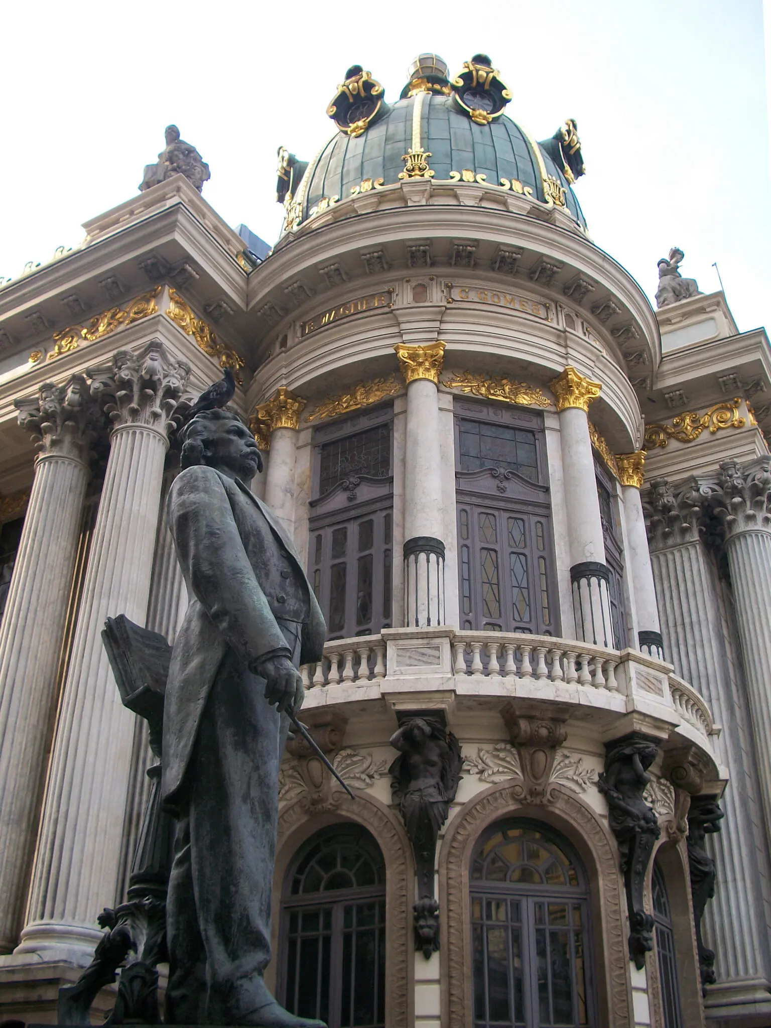 Edifício neoclássico com estátua de bronze em primeiro plano.