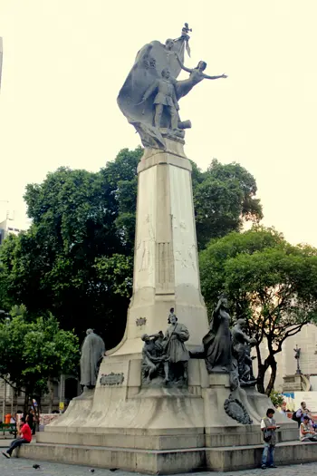 Estátua monumental em espaço público, com figura levantando braços.