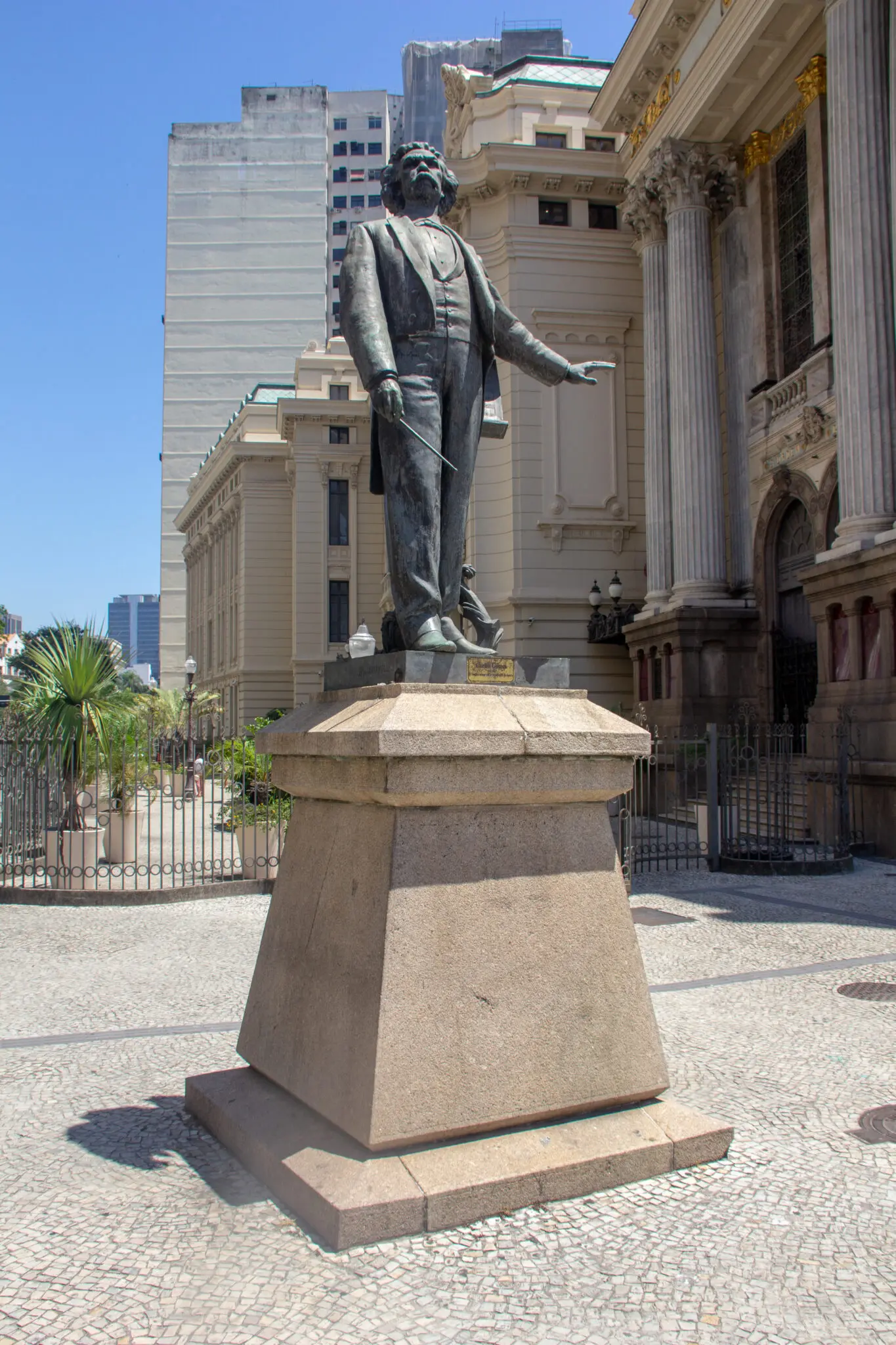 Estátua masculina em traje formal diante de edifícios clássicos e modernos.