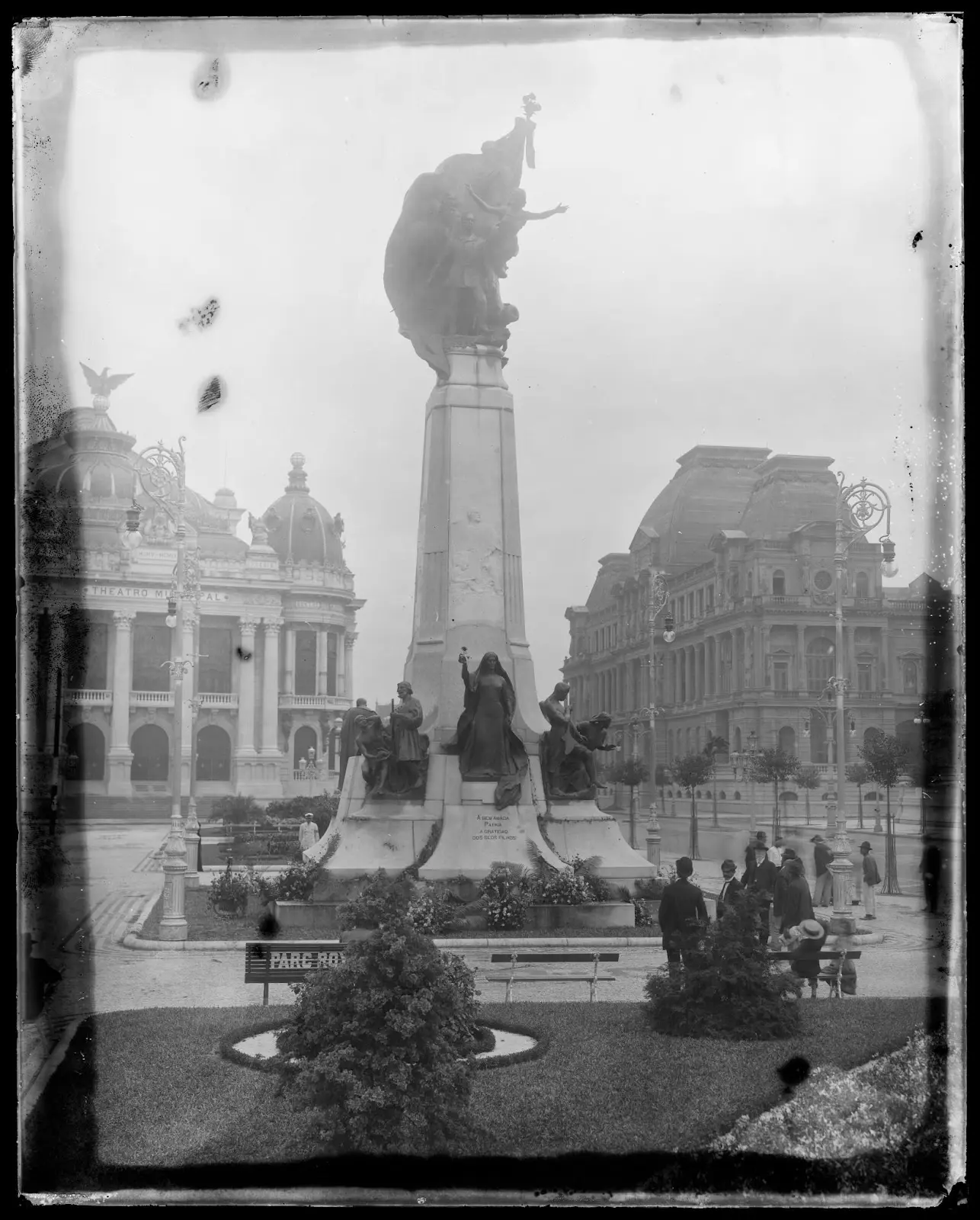 Estátua monumental em praça histórica com edifícios ao fundo.
