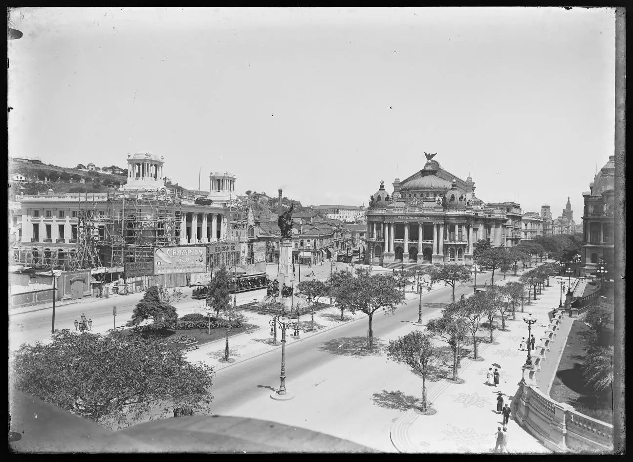 Praça urbana com teatro ornado e estátua central.