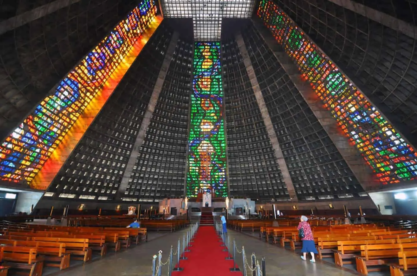 Interior da Catedral Metropolitana do Rio de Janeiro, com bancos de madeira e vitrais coloridos.