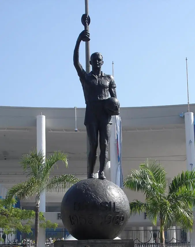 Estátua de atleta erguendo troféu em frente ao Maracanã, com esfera marcando anos 1958 e 1962.